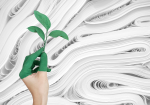 A hand with green painted fingers holds a small plant against a background of paper rolls