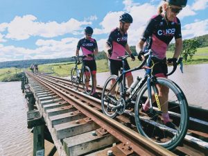 Cyclists walk over train track bridge pushing bikes beside them