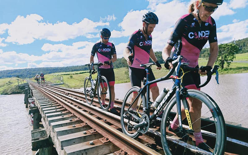 Three cyclists walk across train track above flooded highway