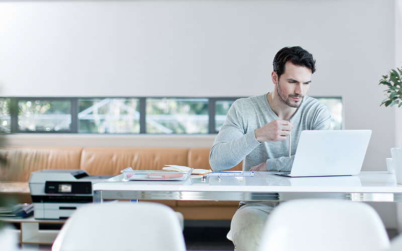 Man sits at desk with Brother printer in background