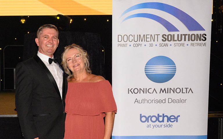 Barry James and Linda smiling next to Document Solutions Australia and Brother Australia banner at the 2021 Gold Coast Health Golden Gala Awards.
