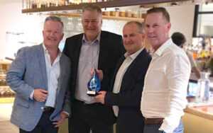 Document Solutions Management Team Alan Thompson, Colin Wheeler and Craig McHenry stand smiling with Konica Minolta Australia COO accepting a token of achievement for 21 years of business