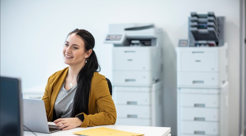 woman smiling while sitting in front of an office printer