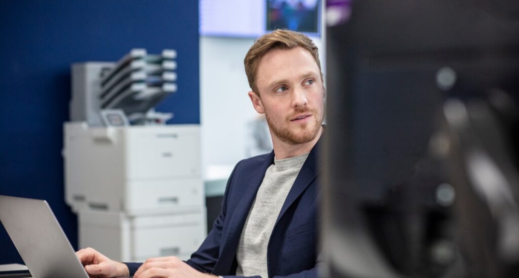 man working on a laptop connected to an office printer